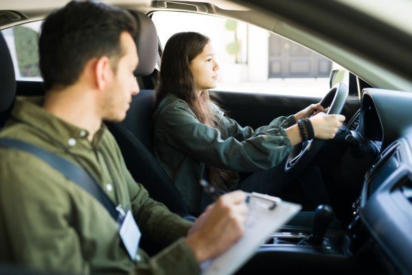Pretty adolescent girl driving a car with the seatbelt. Male instructor telling some instructions and directions to a teen girl during a lesson