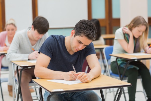 Estudiantes sentados en una sala de exámenes realizando un examen