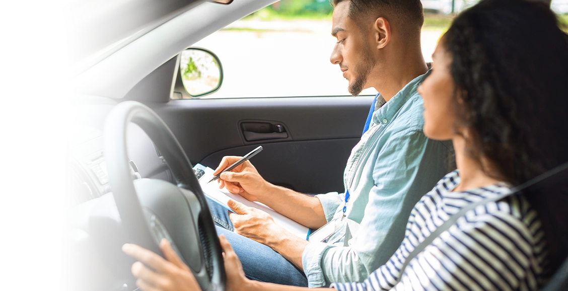 A man and woman seated in a car, taking notes on a clipboard while participating in a driving test in Texas.