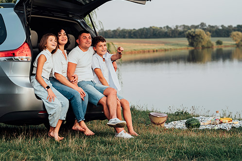 A family relaxes in the trunk of their car by the water, enjoying a sunny day and the beauty of the outdoors.