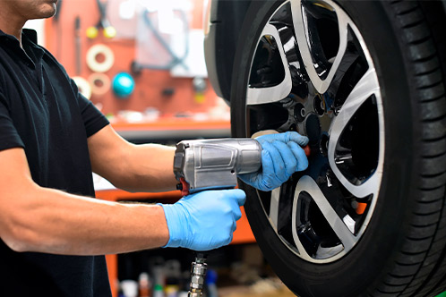 A man uses a tire iron to fix a tire, illustrating key car maintenance tips for teen drivers in Texas.