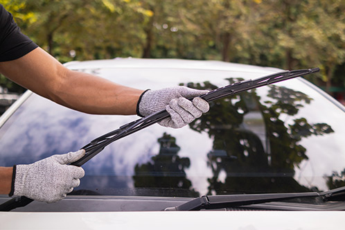 A man uses a windshield wiper to clean a car's glass, highlighting important maintenance tips for Texas teen drivers.