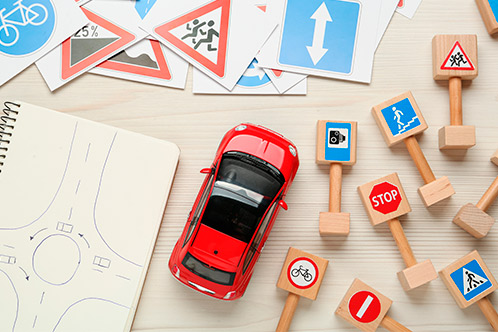 A colorful toy car rests on a table with multiple traffic signs, representing elements of a Texas driving course.