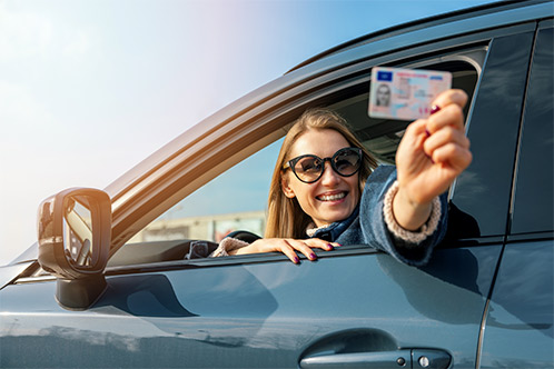 A woman wearing sunglasses holds a drive license, symbolizing online payment for a Texas-approved driving course.