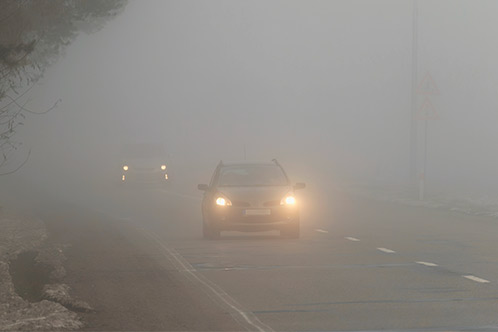 Morning fog envelops cars driving down a road, highlighting the importance of safe driving in Texas during fall.