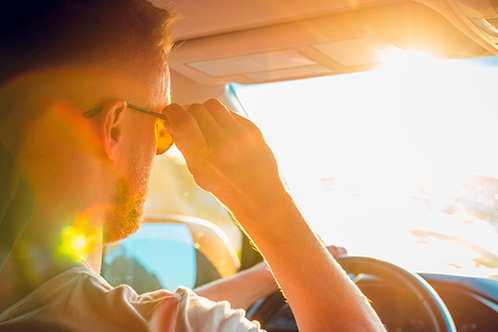 A man wearing sunglasses is behind the wheel of a car, highlighting safe driving tips for Texas fall weather.