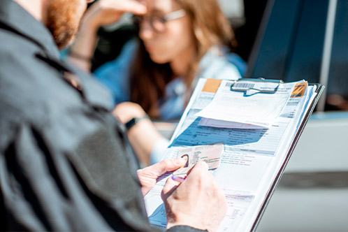 A man in a car takes notes on a clipboard, studying U-Turn laws relevant to new Texas drivers.