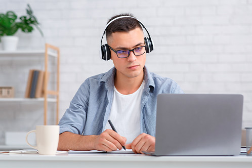 A man wearing glasses and headphones works intently on his laptop, seeking guidance after failing the Texas DPS Written Exam.