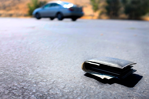 A wallet resting on the ground next to a car, indicating it may have been dropped by someone nearby.