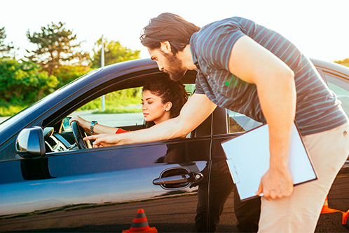 Inside a car, a man with a clipboard talks to a woman about saving money and licenses through Texas Defensive Driving Online.