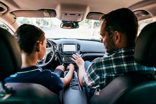 A man and a boy in the back seat of a car, highlighting the benefits of defensive driving for Texas car insurance savings.