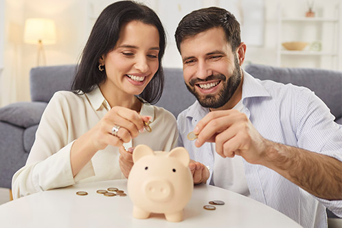 A smiling couple adds coins to a piggy bank, symbolizing savings and financial planning for car insurance.