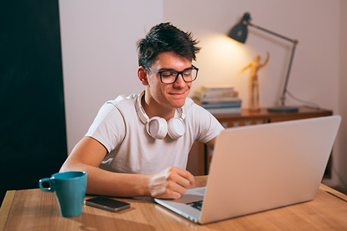 A man with glasses sits at a table using a laptop, highlighting the Texas Adult Drivers Ed available this weekend.