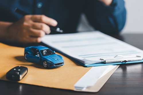 A man drafting a car insurance policy on a desk, accompanied by a toy car, highlighting Texas defensive driving benefits.