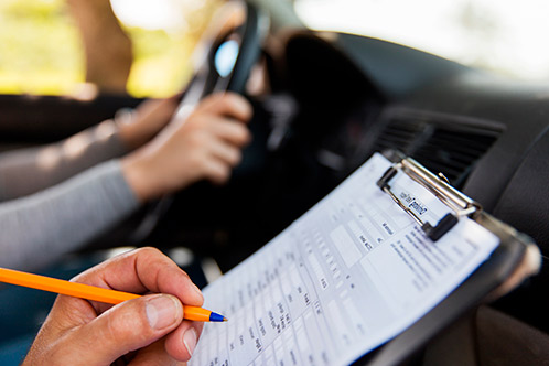 A driver writes on a clipboard, demonstrating the challenges of multitasking during Texas Adult Drivers Ed training.