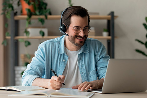 A man wearing a headset works at a desk with a laptop, studying the Texas Parent Taught Drivers Ed checklist.