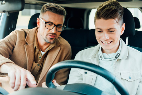 Inside a car, a man looks at the steering wheel while a boy sits beside him, highlighting Texas Parent Taught Drivers Ed.