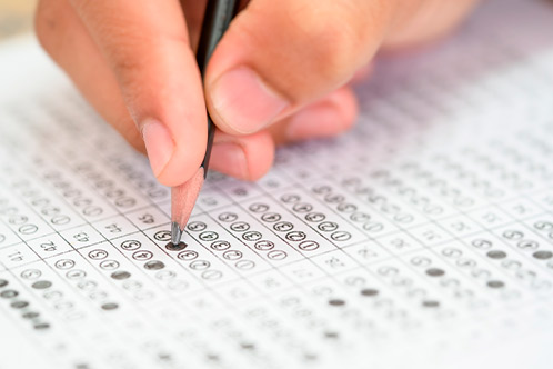 A hand holds a pencil, filling in bubbles on a standardized test answer sheet. The focus is on precision and concentration, conveying a sense of focus.