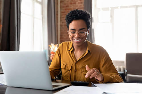 A woman smiling while using her laptop to complete her online Texas driver application.