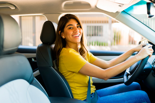 Excited young woman making eye contact and smiling while driving home her new car