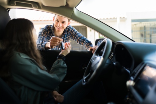 Handsome father smiling and giving her teen daughter the car keys. Adolescent girl ready to start driving after getting her driver's license