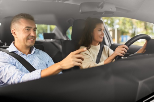 driver courses and people concept - car driving school instructor teaching young woman to drive