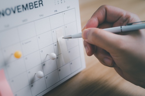 Close-up of woman hand holding pen marking an important date on desk calendar, Scheduling planning, Business appointment, Meeting schedule, travel planning. selective focus